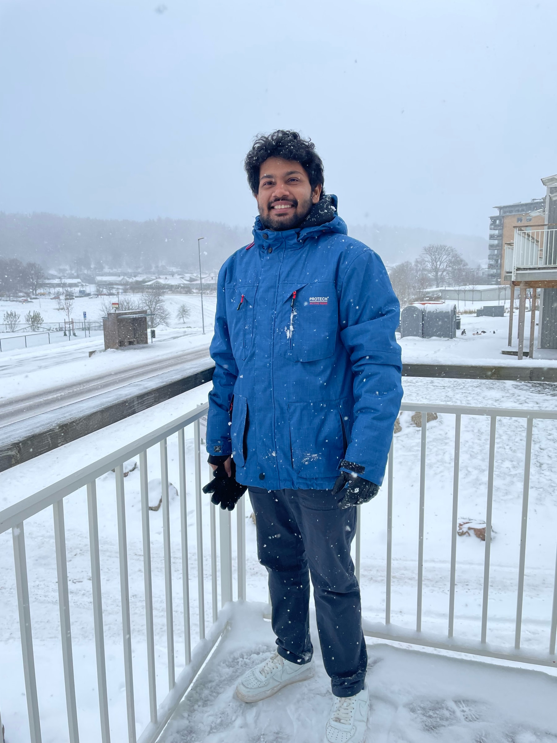 Yesith smiling on a snowy balcony in a blue winter jacket